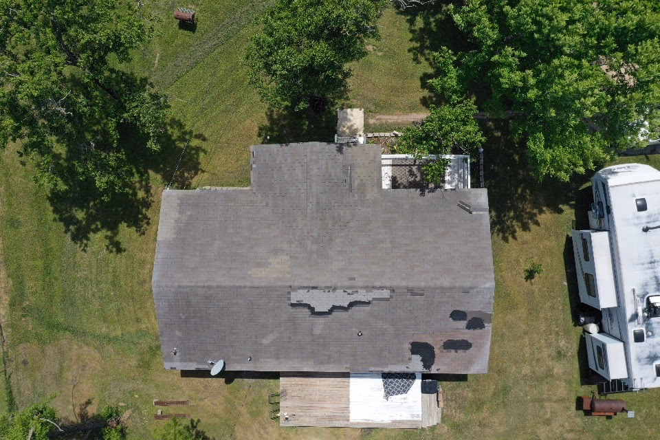 Aerial drone view of an aged gray shingle roof with a damaged area and dark patch repairs in Austin, TX