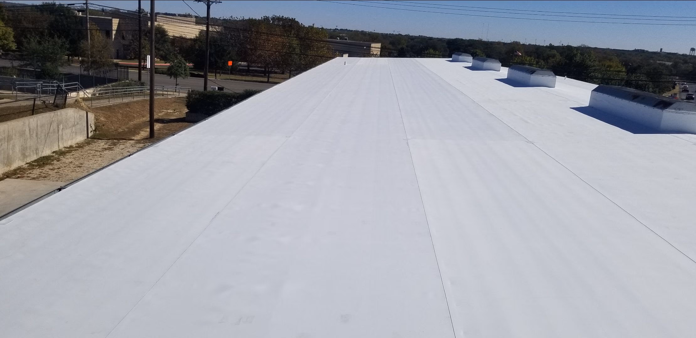 The same commercial building after the recover, fully covered in bright white membrane with wrapped ridge vents in Austin, TX