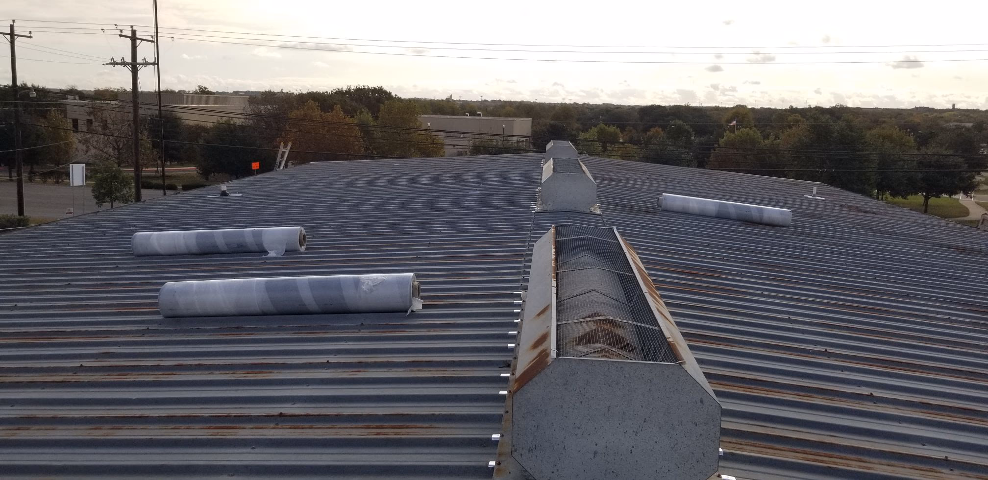 Rusted corrugated metal commercial roof with membrane rolls staged on top before a roof recover in Austin, TX