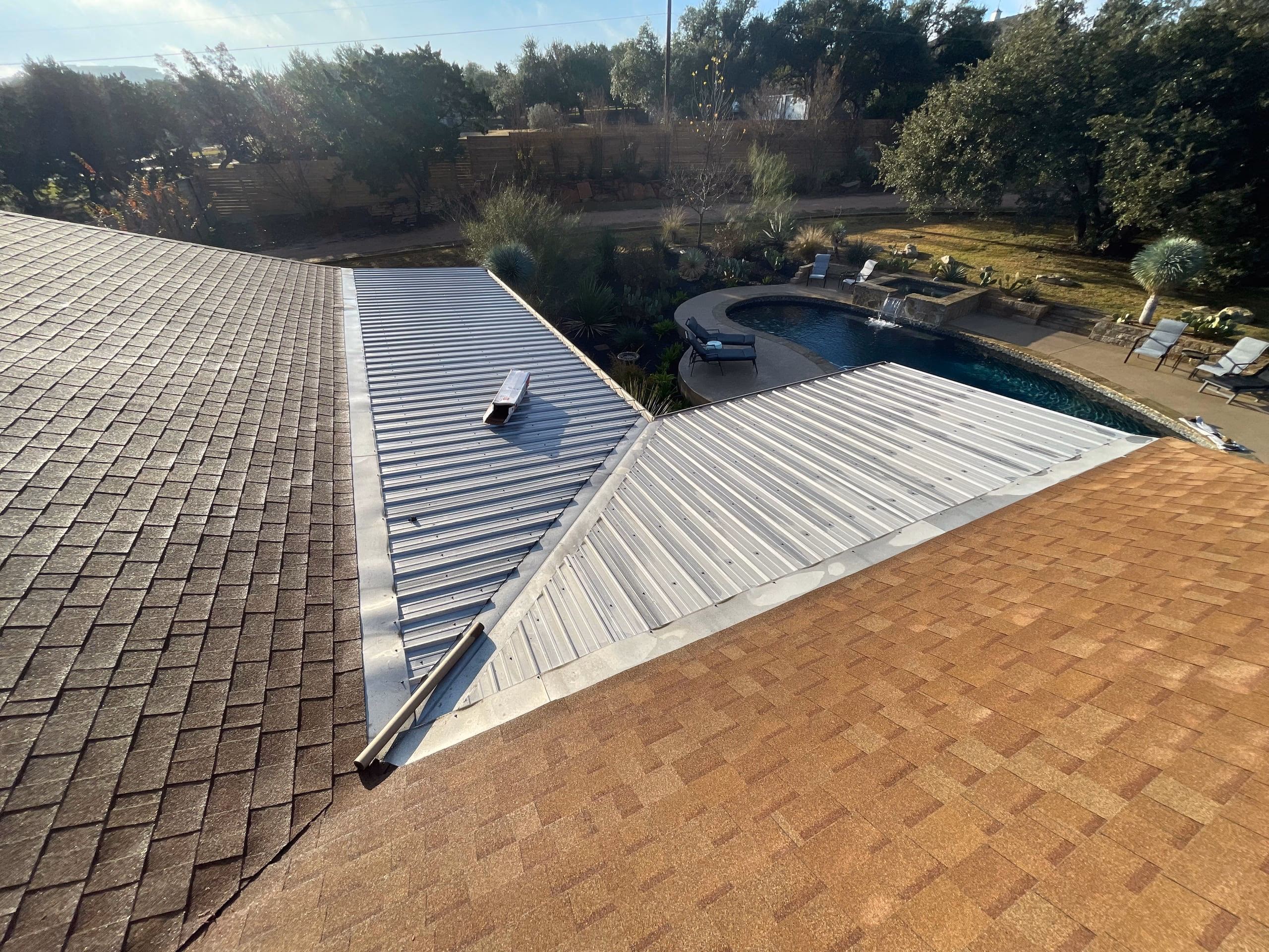Aged brown shingles and weathered silver metal roof panels on a home overlooking a backyard pool before replacement in Austin, TX