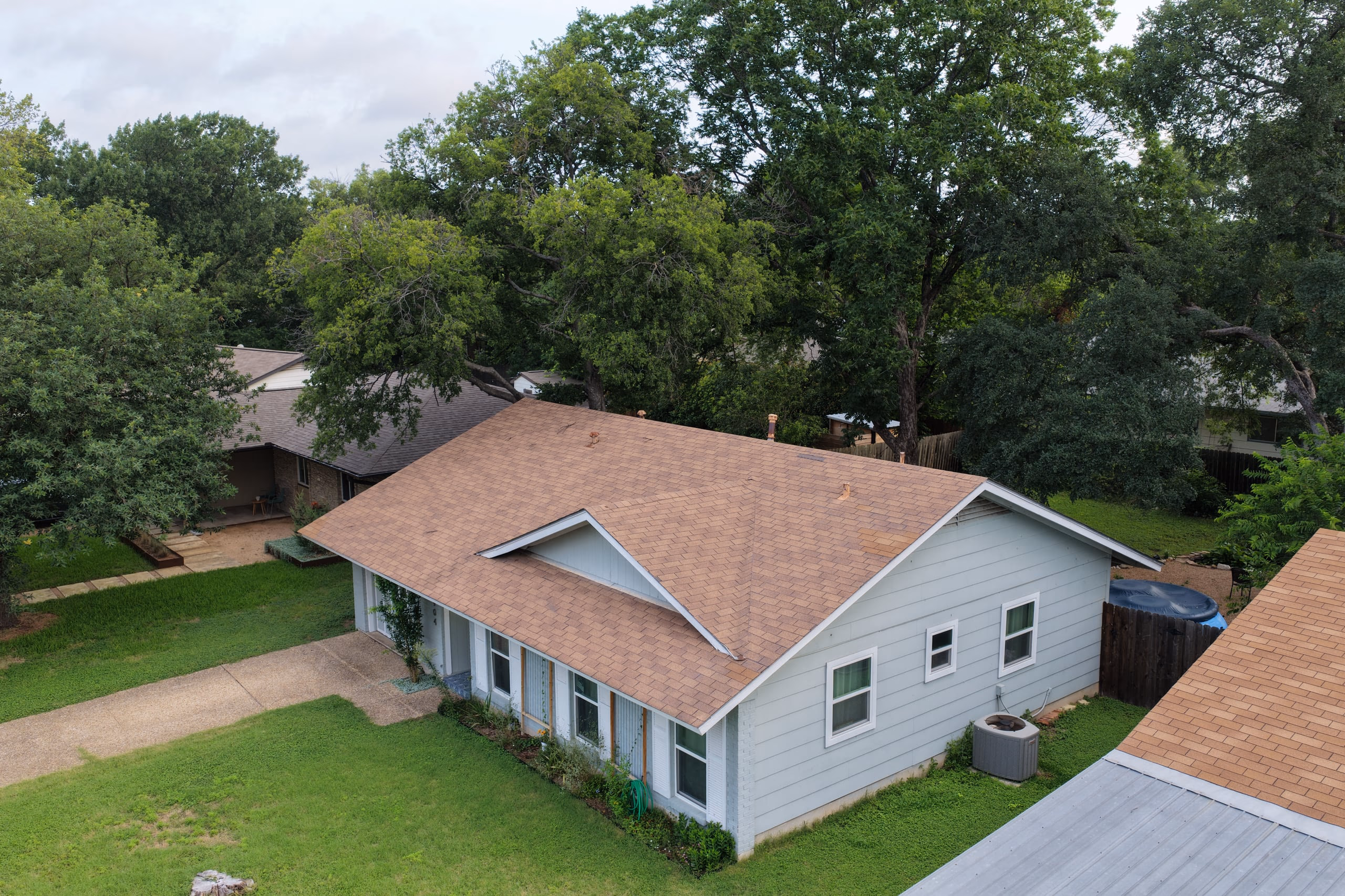 Single story home with faded brown shingles and a visible patch repair before roof replacement in Austin, TX