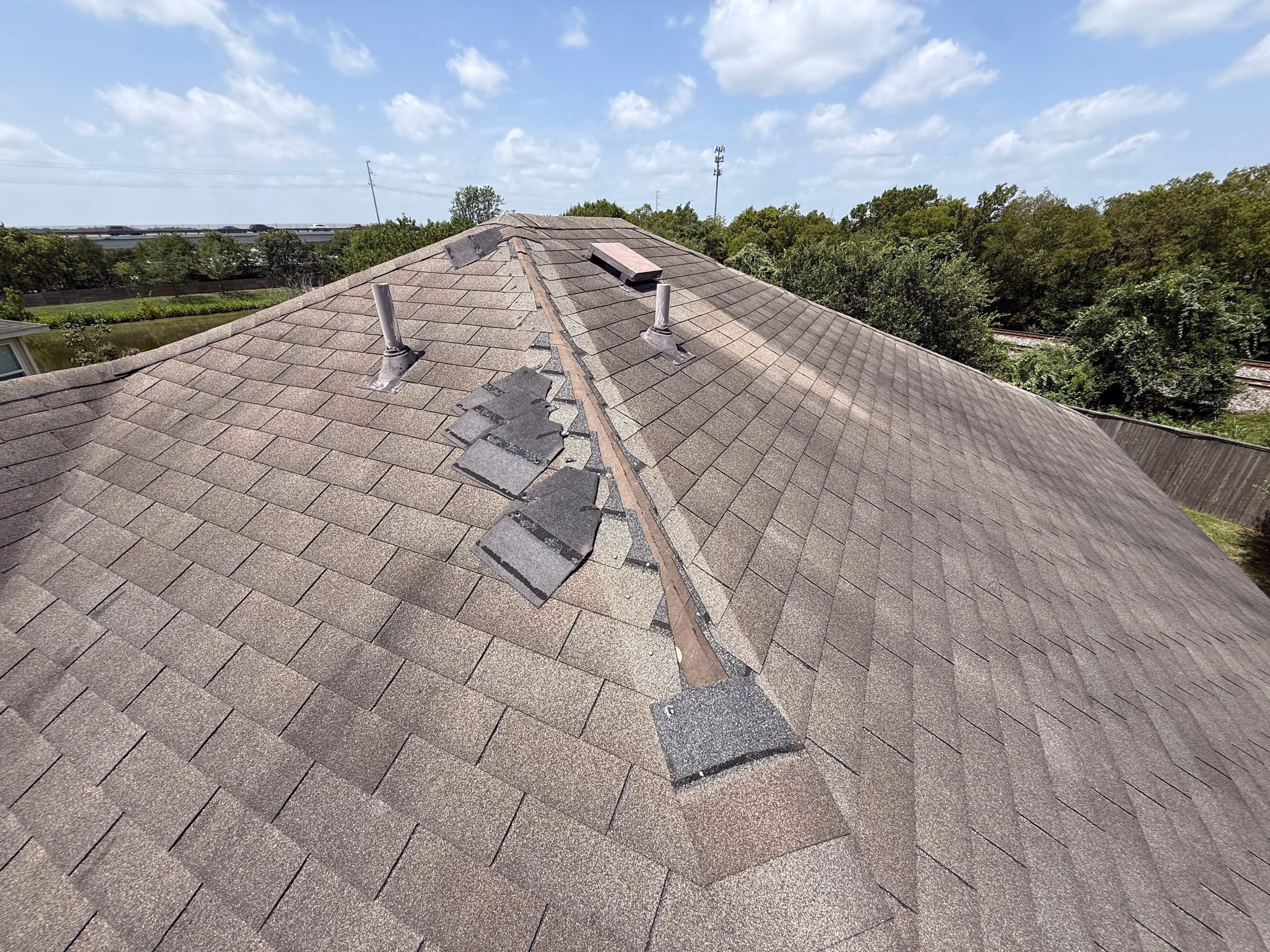 Broken shingle tabs scattered along the hip with exposed felt after wind damage on an Austin, TX roof