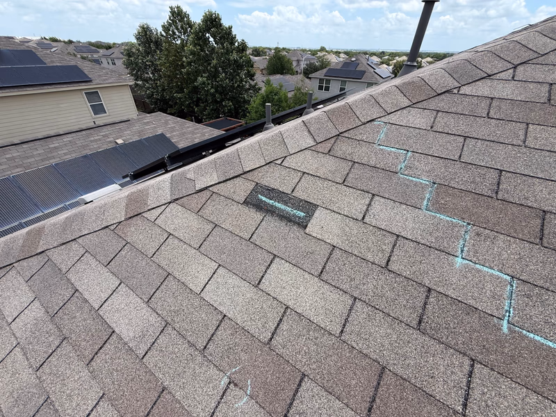 Teal chalk marks and a replaced shingle documenting completed storm damage roof repair work on a tan roof in Austin, TX