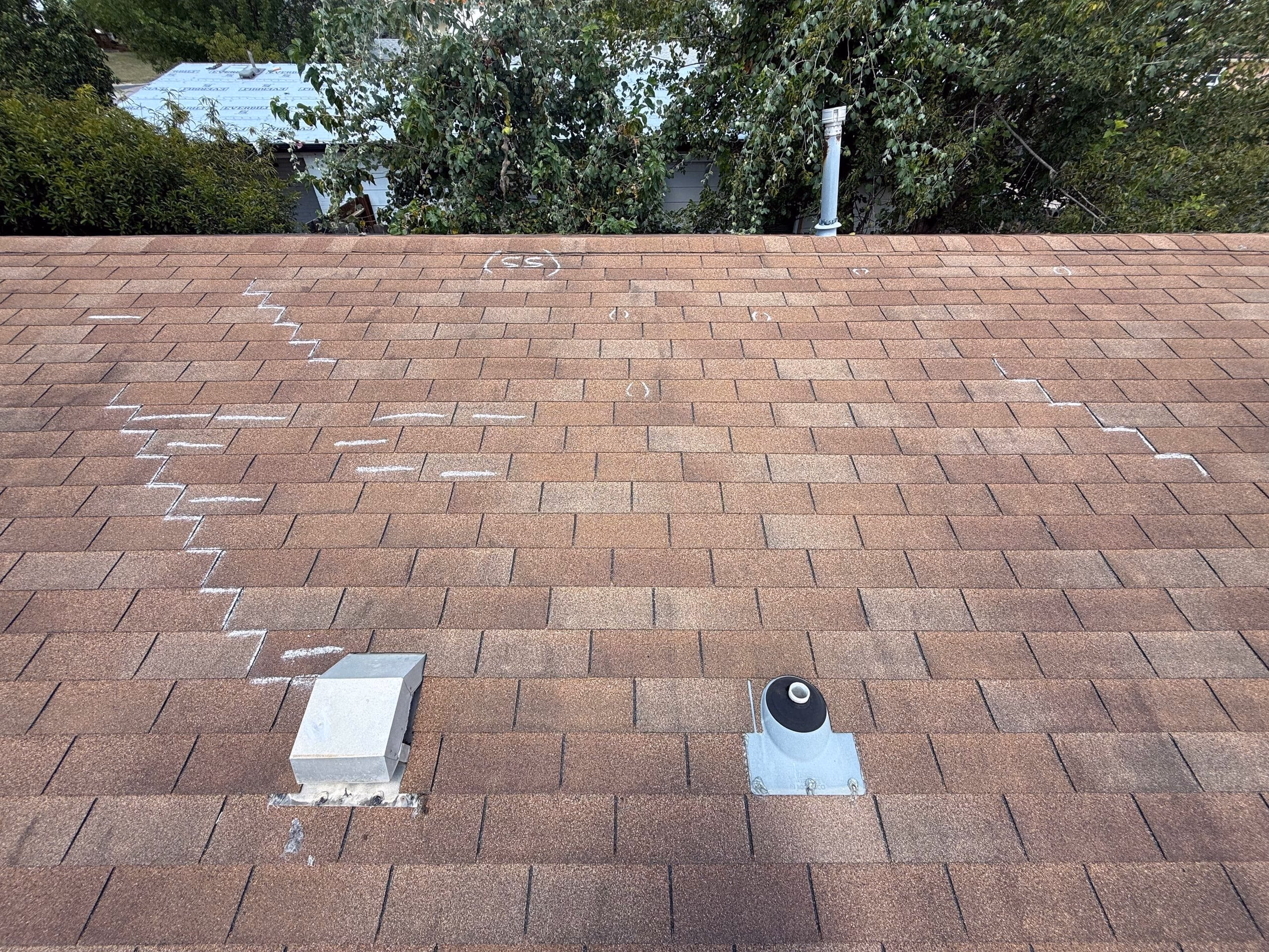 Chalk marks tracing damaged shingle courses near a box vent and pipe boot during a storm inspection in Austin, TX