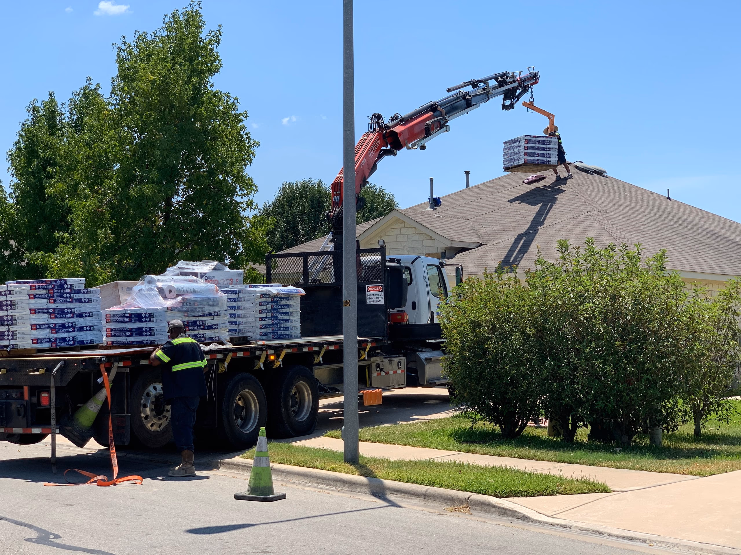 Boom crane loading GAF Timberline HD shingle bundles onto a roof on replacement day in Austin, TX