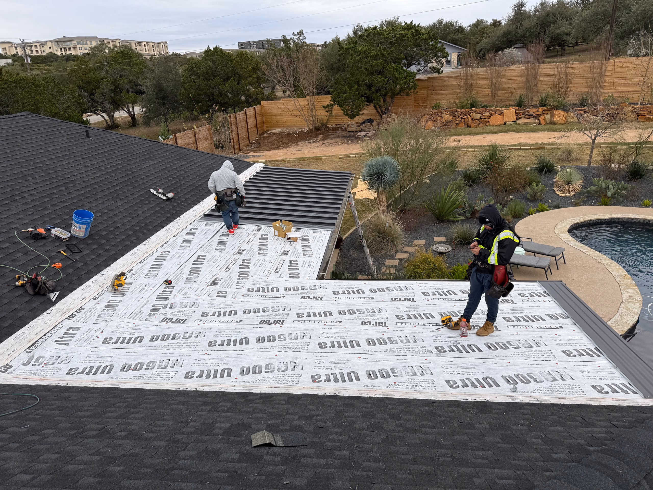 Roofers installing dark bronze metal panels over high temperature self adhering underlayment during a metal roof replacement in Austin, TX