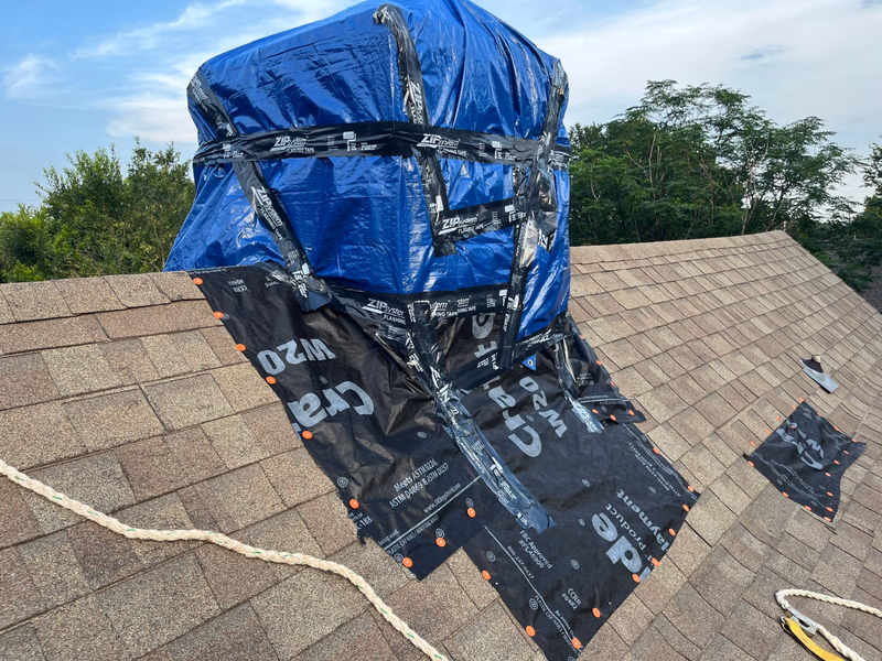 Emergency roof tarping by Austin Roofing Company: chimney sealed with a heavy-duty tarp, ZIP System flashing tape, and cap-nailed synthetic underlayment on an Austin shingle roof