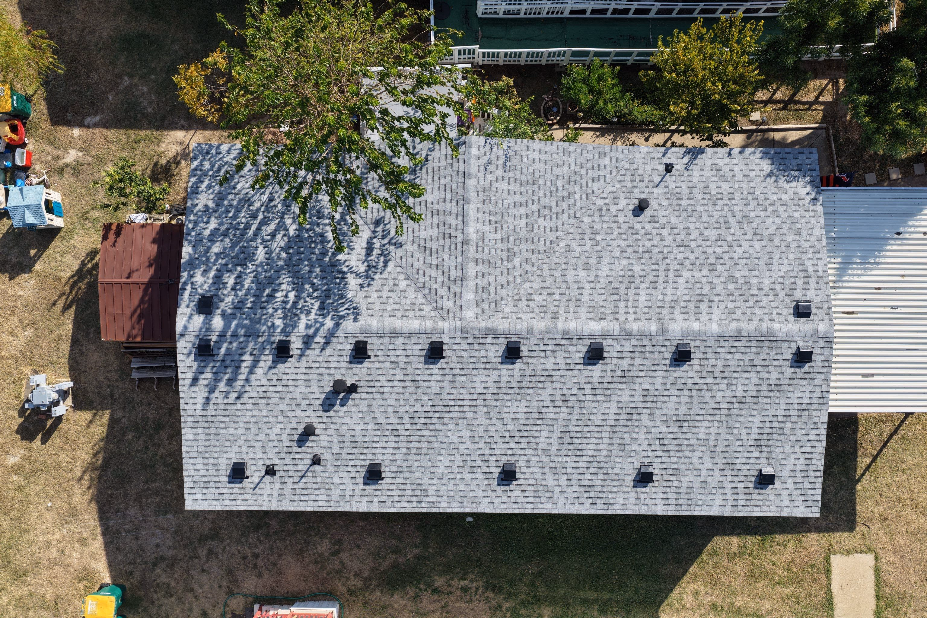 Aerial view of a completed shingle roof replacement shaded by a large tree in Austin, TX