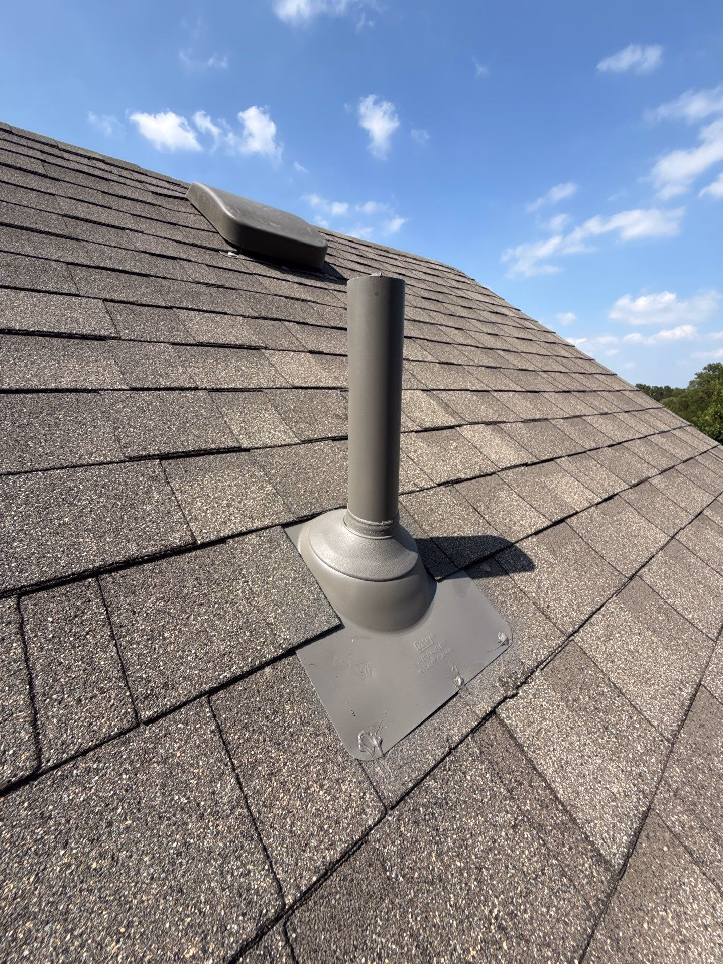 New flue pipe with storm collar and metal base flashing installed on an asphalt shingle roof in Austin, TX