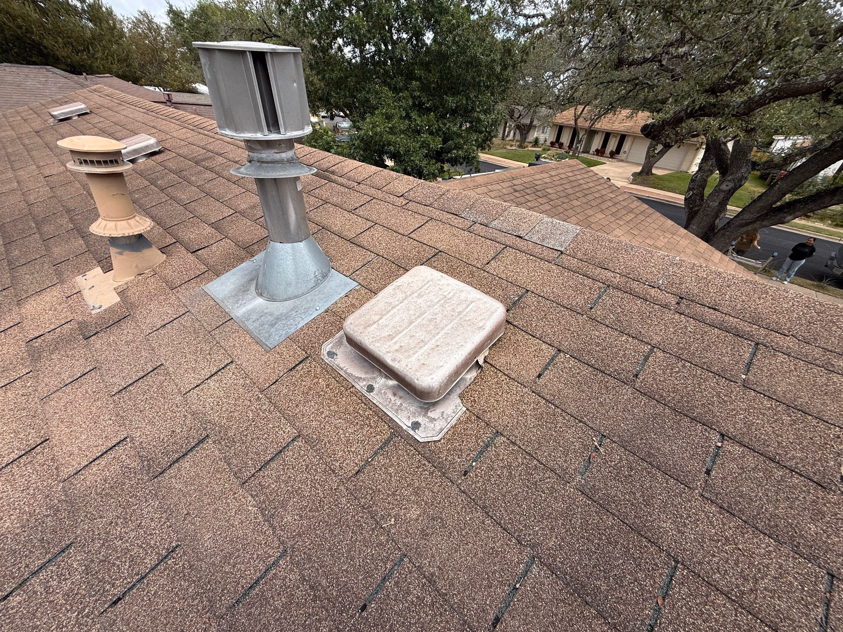 Hail dents visible on a metal turtle vent on top of a tan shingle roof in Austin, TX