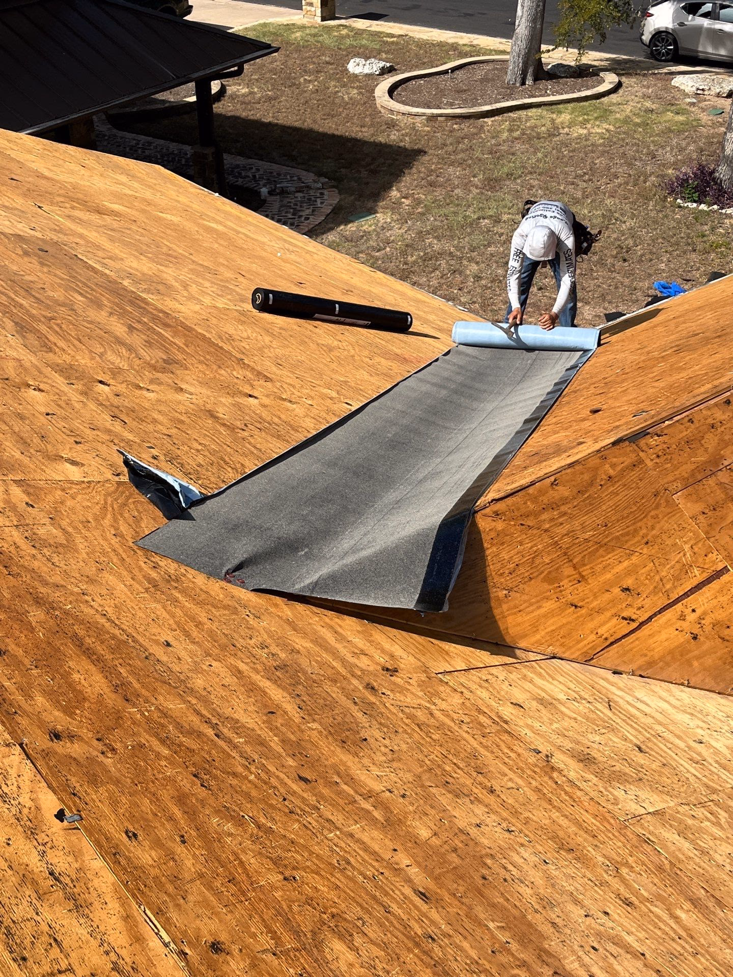 Worker fitting gray synthetic underlayment over bare plywood decking at a hip during an Austin, TX roof replacement