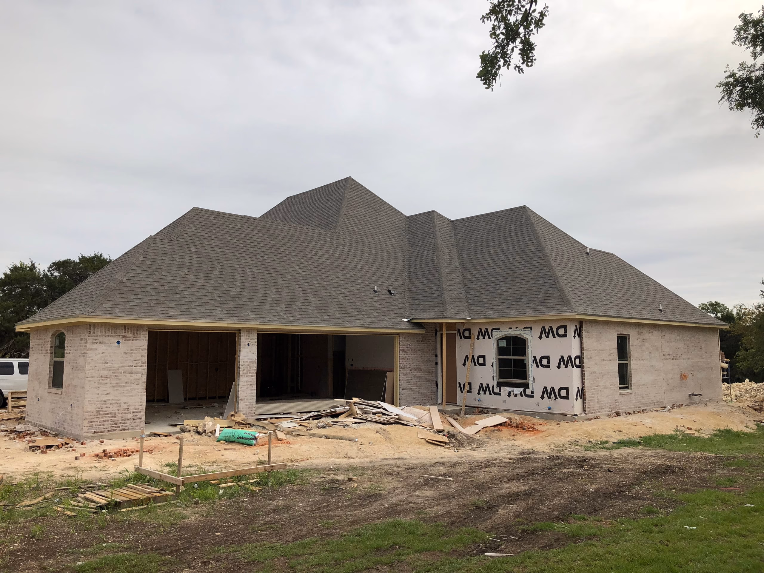Newly installed gray architectural shingle hip roof on a white brick home still under construction in Austin, TX