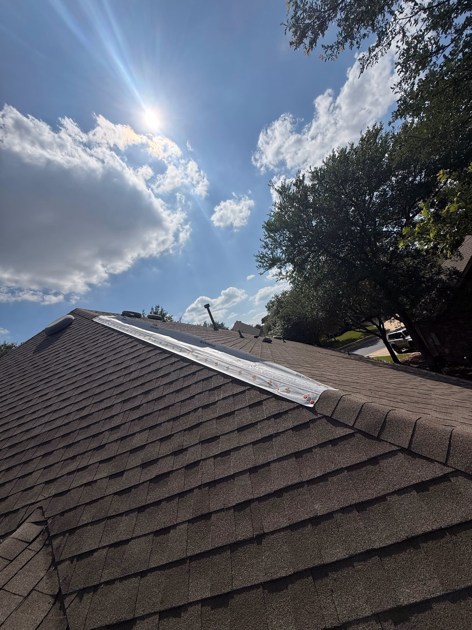 White ridge vent material laid along the ridge of a dark brown shingle roof during a repair in Austin, TX