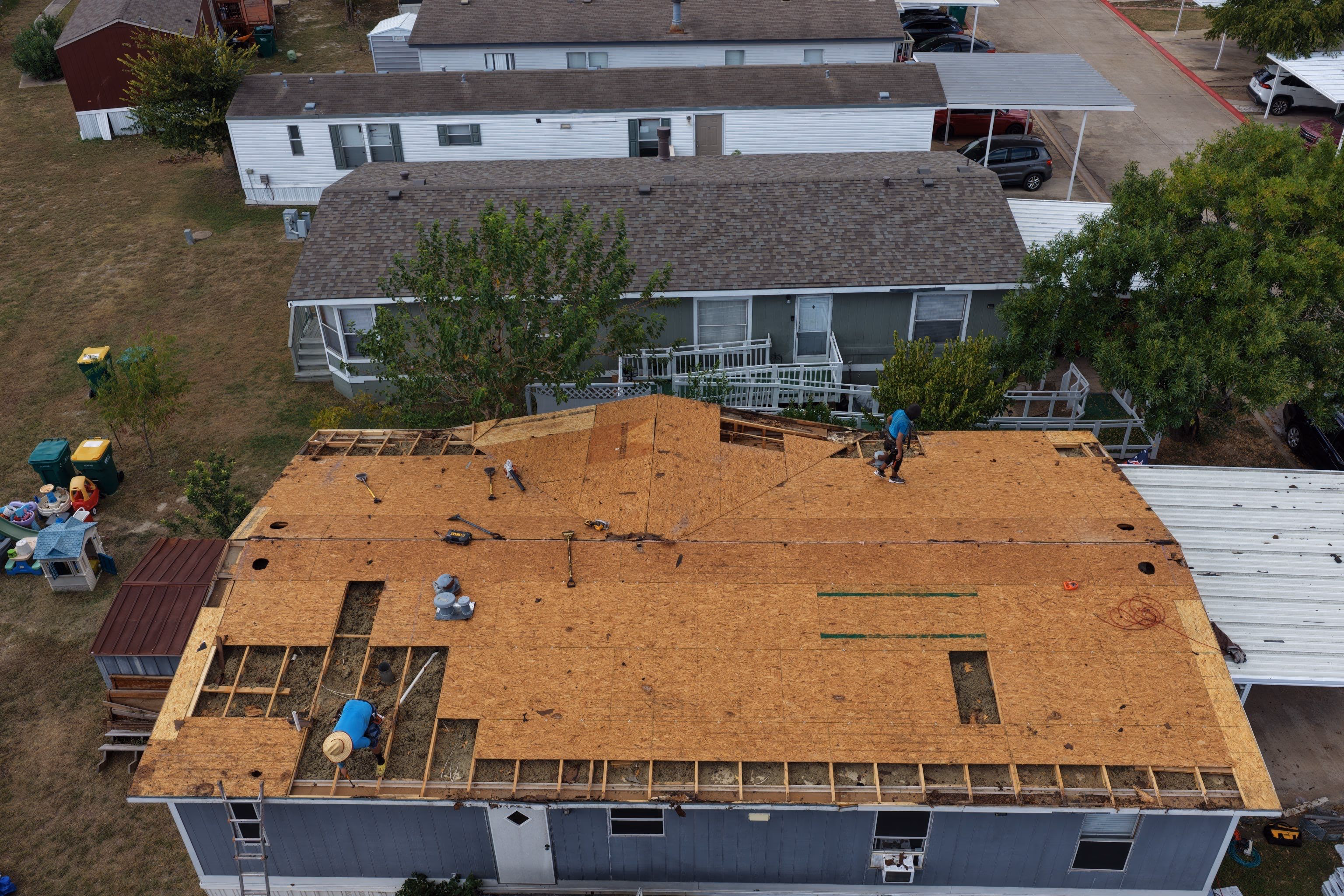 Roofers installing new plywood decking over open rafters during a roof replacement in Austin, TX