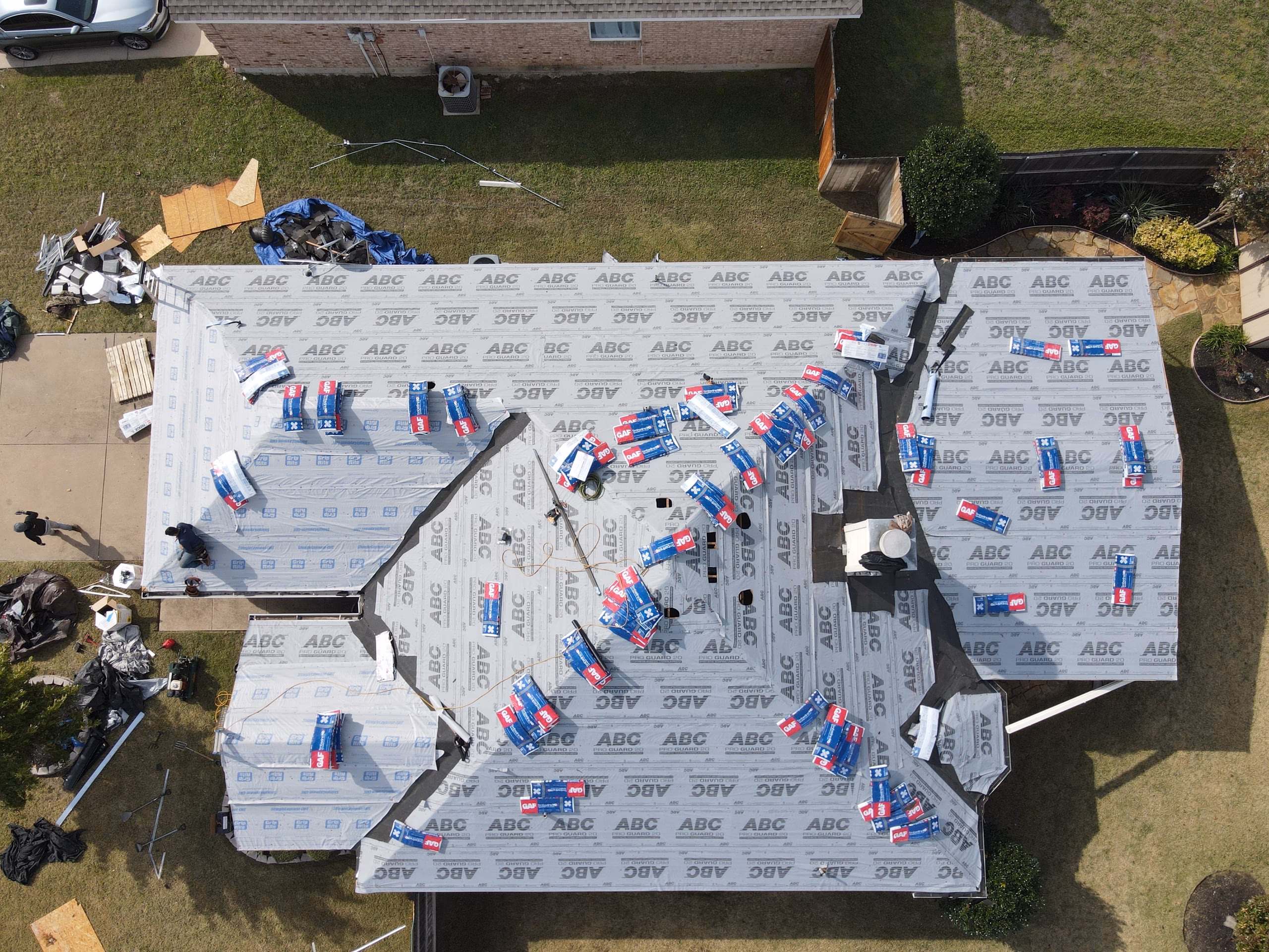 Drone view of a roof covered in gray synthetic underlayment with shingle bundles staged across the slopes in Austin, TX