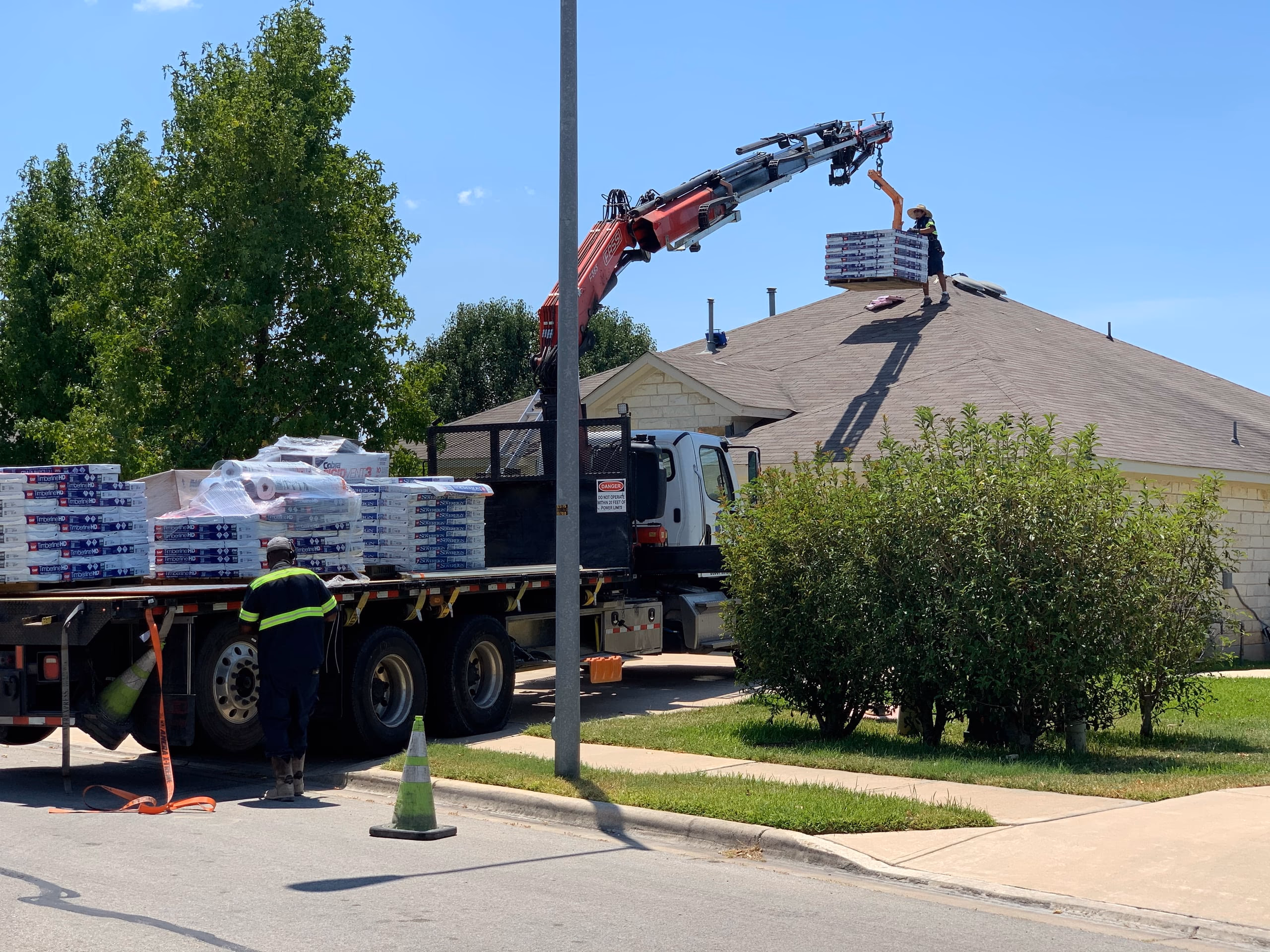 Boom crane lifting pallets of shingle bundles from a delivery truck onto the roof of a limestone home in Austin, TX