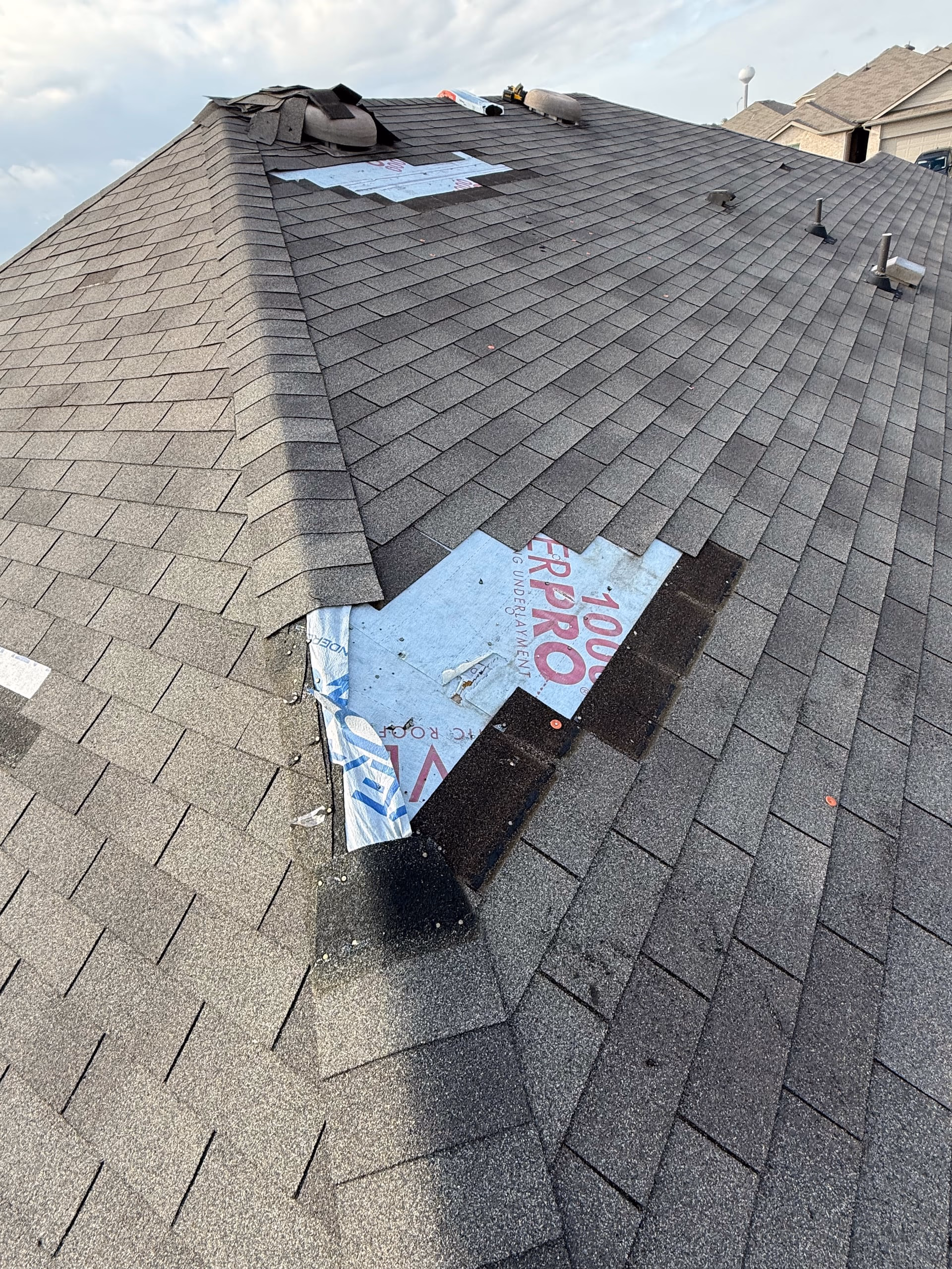 Shingles removed from a hip roof section showing printed synthetic underlayment during a roof repair in Austin, TX