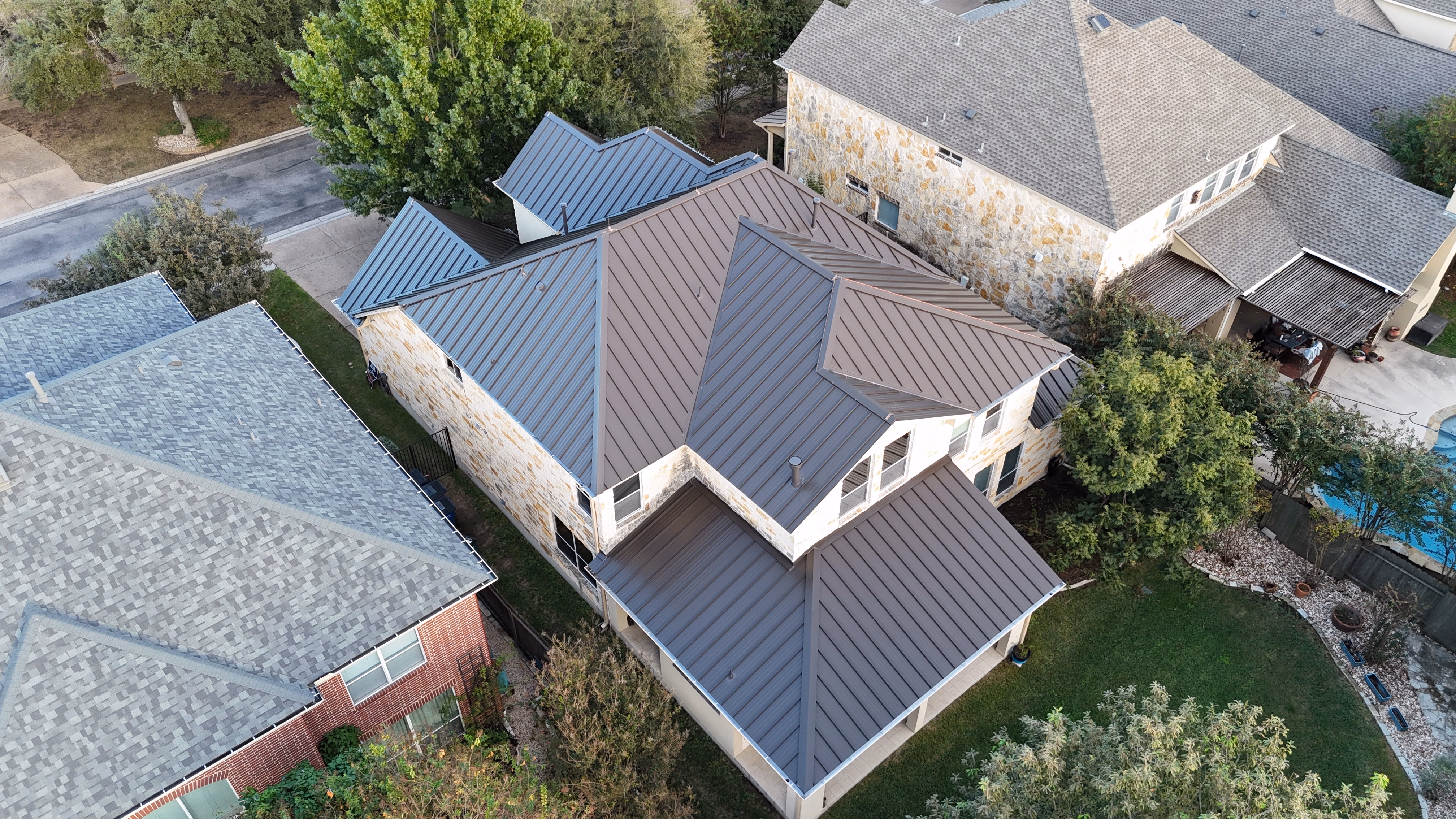 Aerial drone view of a dark bronze standing seam metal roof installed on a limestone home in Austin, TX