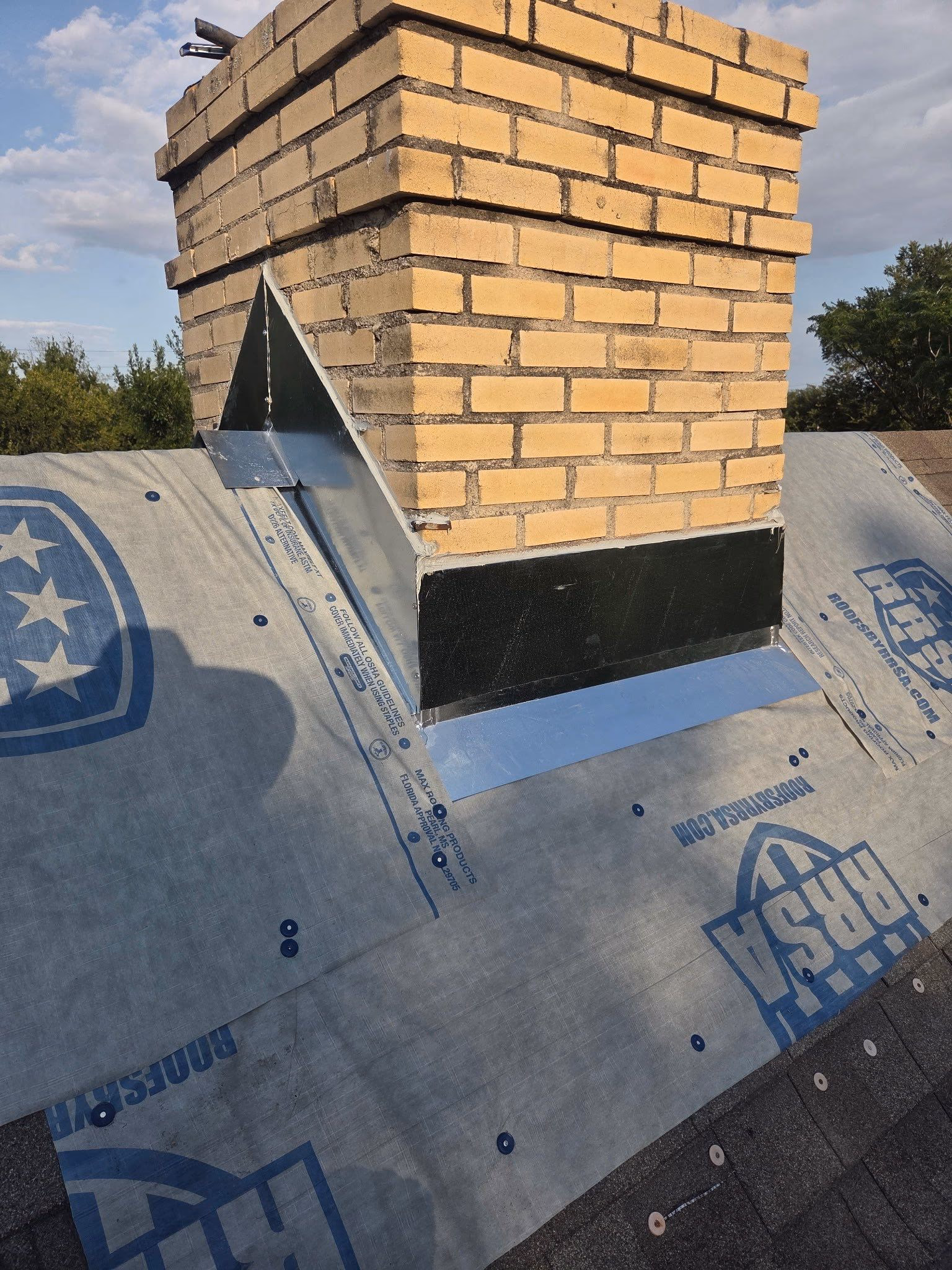 New step flashing and synthetic underlayment installed around a yellow brick chimney during a roof replacement in Austin, TX