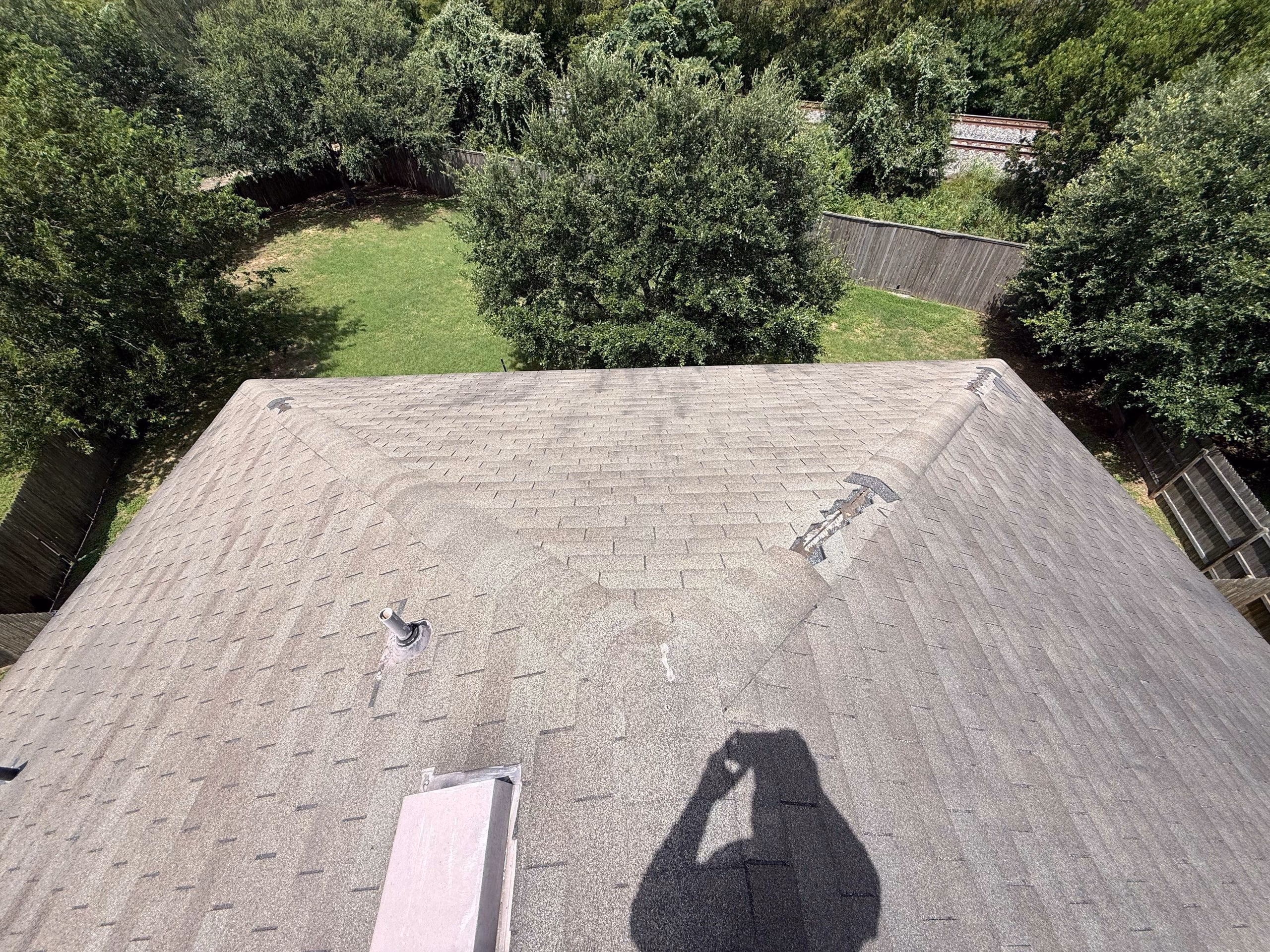 Damaged hip shingles on a tan asphalt roof after a storm in Austin, TX
