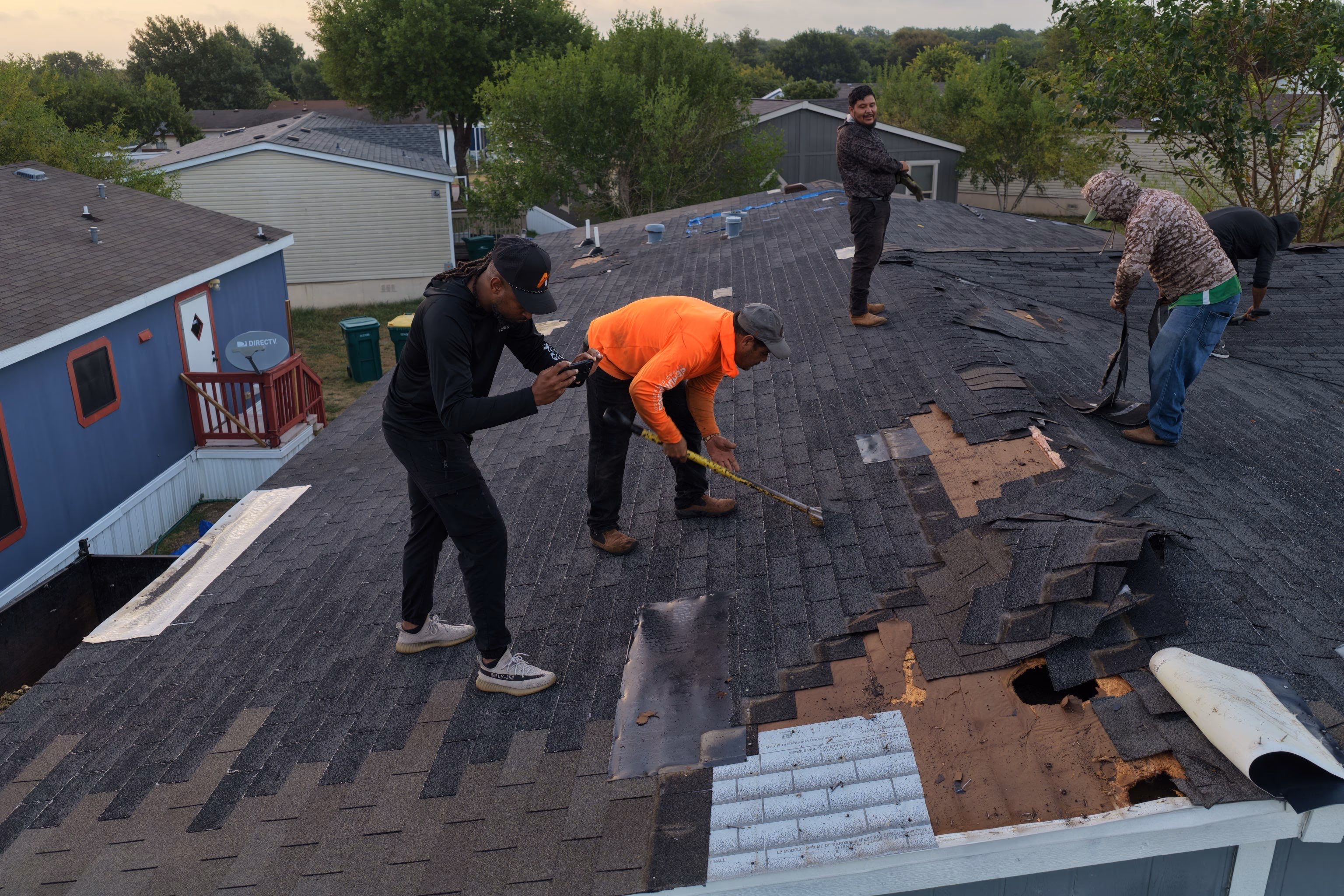 Crew tearing off old shingles down to bare decking during a roof replacement in Austin, TX