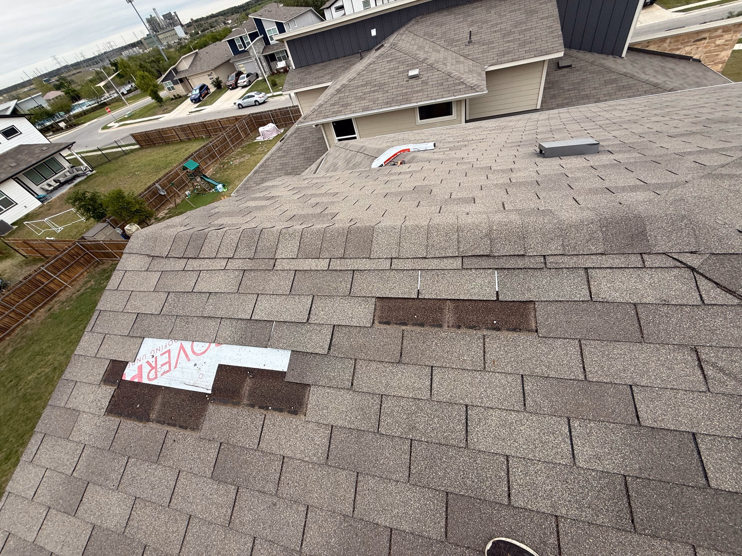 Missing shingles blown off by wind exposing synthetic underlayment on a tan shingle roof in Austin, TX