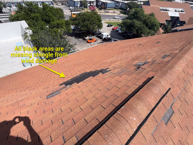 Annotated inspection photo showing black patches of missing shingles from wind damage on a brown roof, documented for an insurance claim in Austin, TX
