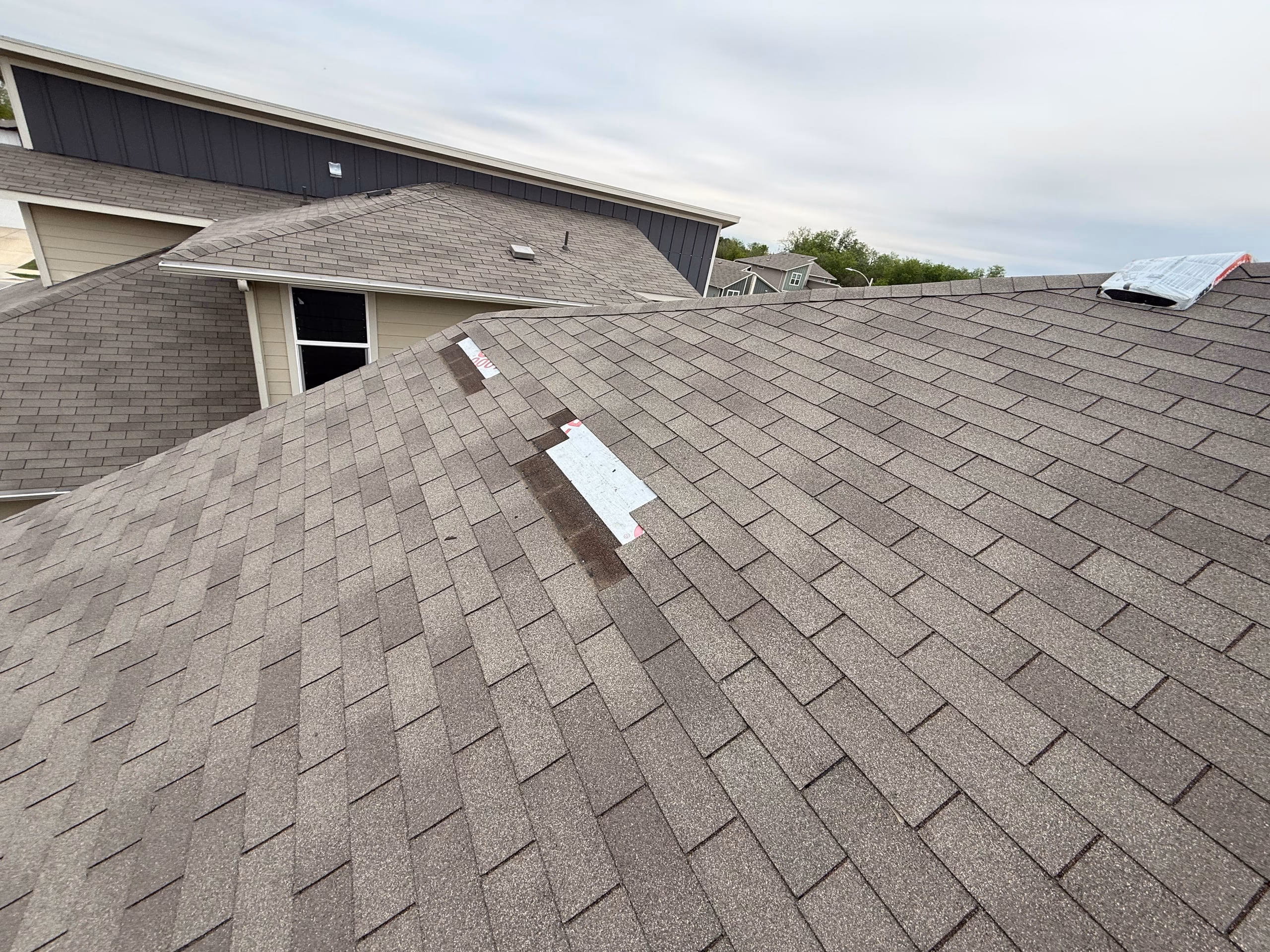 Wind damaged roof slope with shingles torn off near the ridge and underlayment exposed on an Austin, TX home