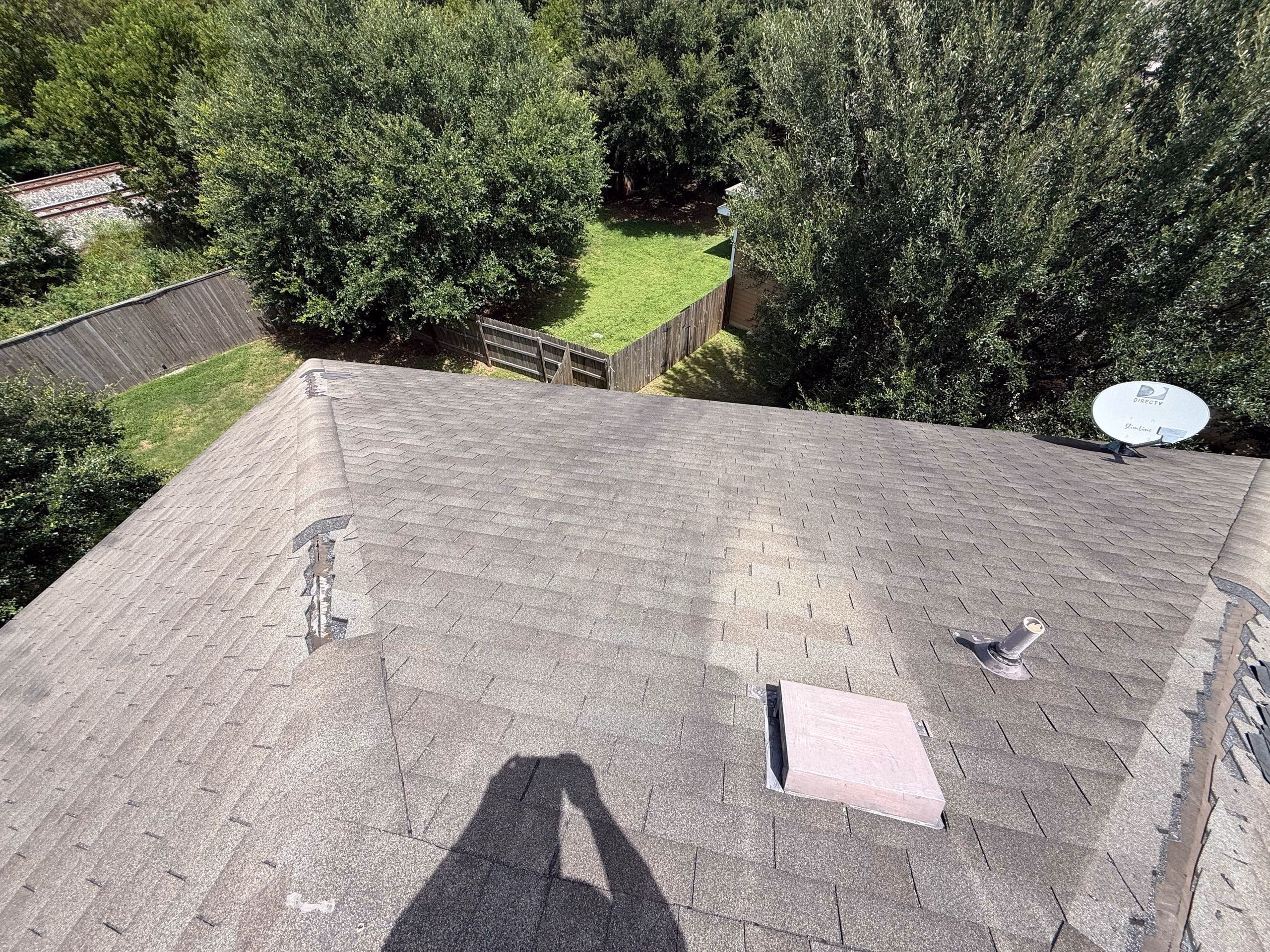 Wind torn shingles at a roof hip with an older patch exposed underneath on an Austin, TX home